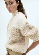 Sweater de punto grueso color beige con diseño patchwork. Tiene cuello alto y mangas largas.