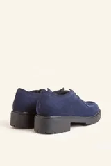 Zapato tipo wallabee de gamuza azul con costuras blancas a la vista y suela de goma negra con plataforma.