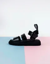 Sandalias negras charoladas con plataforma, tiras anchas y hebilla al tobillo.