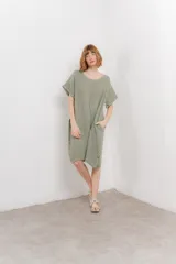 Vestido corto color verde oliva, confeccionado en lino, con corte recto y mangas cortas. Presenta bolsillos laterales y botones decorativos en los laterales.