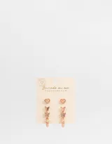 Set de tres pares de aros bañados en oro rosa: aros pasantes con forma de corazón, aros colgantes con forma de mariposa con strass y aros tipo argolla con textura. Todos con cierre a presión.