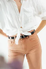 Cinturón negro de cuero charol con hebilla metálica plateada y ojales metálicos.