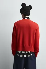 Cárdigan rojo de punto con cuello redondo, manga larga y cierre frontal con botones. Tiene un parche de Minnie Mouse en el pecho.