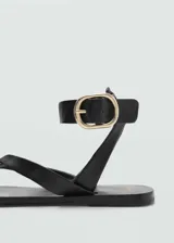 Sandalias de cuero negras con tira entre los dedos y pulsera al tobillo con hebilla dorada.
