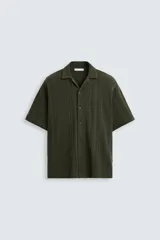 Camisa verde militar de corte relaxed fit, con cuello bowling, manga corta, bajo con aberturas laterales y cierre frontal de botonadura.
