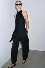 Top negro satinado con cuello halter, manga sisa y bajo asimétrico. Cierre en la espalda.