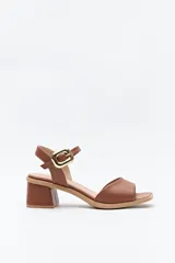 Sandalia color marrón con pulsera al tobillo y hebilla metálica cuadrada. Presenta una capellada ancha que cubre el empeine y taco medio ancho.