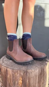 Botas Chelsea de cuero color marrón, con elástico lateral, suela negra gruesa y pespuntes blancos.