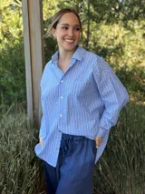 Camisa holgada a rayas verticales color beige y blanco, con cuello clásico, manga larga, bolsillo en el pecho y cierre frontal con botones nacarados.