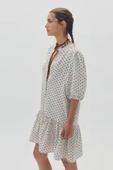 Vestido corto color blanco con estampado de lunares negros, escote en V, mangas cortas abullonadas y falda con volantes.