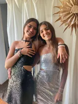 Vestido corto asimétrico con un hombro descubierto y dos breteles finitos que se atan cruzados en la espalda. El vestido es de lentejuelas plateadas y tiene un corte en la cintura.