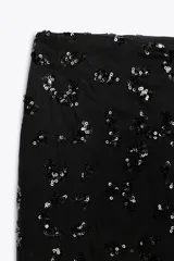 Pantalón negro de tiro alto con lentejuelas, corte palazzo y cierre frontal con cremallera, botón interior y gancho metálico.