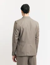 Traje de vestir color marrón topo, compuesto por saco de dos botones con solapa de muesca, dos bolsillos delanteros con solapa y un bolsillo superior. Pantalón de vestir con corte recto y bolsillos laterales. Incluye camisa blanca y corbata azul con lunares blancos.