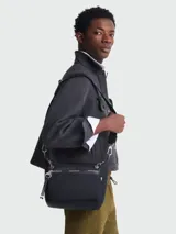 Bandolera negra de nylon reciclado con correa ajustable, cierre superior con cremallera y solapa con botón a presión. Incluye bolsillo frontal con cremallera y apliques metálicos plateados.