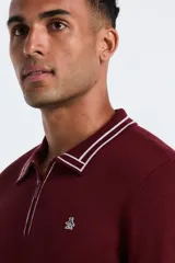 Sweater de punto color bordó con cuello polo y cierre de media cremallera. Presenta detalles de rayas blancas en el cuello y los puños, manga larga y logo bordado en el pecho.
