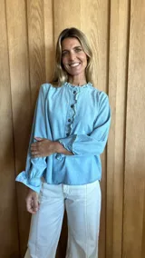 Blusa celeste de mangas largas con puños elásticos, cuello con volados y cierre frontal con botones.