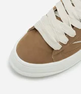 Championes de skate color marrón, confeccionados en material sintético con cordones anchos blancos, suela alta blanca y detalles contrastantes en los laterales.