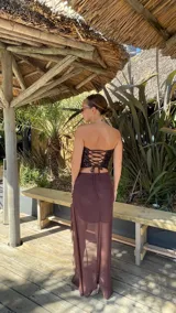 Pollera larga de microtul color marrón, con diseño de transparencias, detalle de fruncido lateral y volados verticales a lo largo de la abertura frontal.