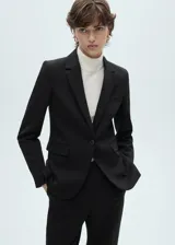 Blazer color beige con solapas de muesca, cierre frontal con un botón, hombros estructurados, corte entallado, forro interior y dos bolsillos de ribete en la parte delantera.