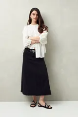 Falda midi de denim negro con tiro bajo, corte evasé, costuras verticales y ruedo desflecado.