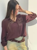Camisa color borgoña con cuello clásico, cierre frontal con botones, bolsillo de parche con encaje en el pecho y mangas largas con lazo en los puños.