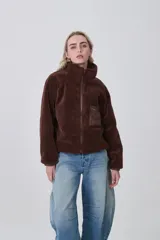 Campera de abrigo color marrón oscuro, confeccionada en tejido de pelo (tipo sherpa o teddy), con cuello alto y cierre frontal. Posee un bolsillo pequeño con cierre en el pecho del lado derecho, con acabado en tela lisa.
