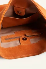 Cartera tipo balde de gamuza color marrón, con correa ajustable decorada con tachas metálicas plateadas y logo grabado en la parte frontal.