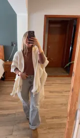 Ruana color crema con flecos en el borde.