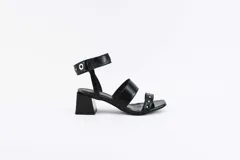 Sandalias negras de cuero con dos tiras sobre el empeine y pulsera al tobillo con ojalillos y tachas. Taco cuadrado de 5 cm.