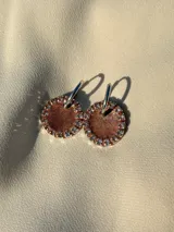 Aros colgantes con forma circular, hechos de resina color lila y borde de strass plateado. El aro es de acero quirúrgico plateado.