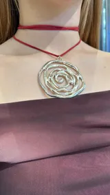 Gargantilla de gamuza roja con dije plateado en forma de espiral.
