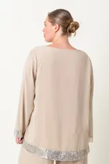Blusa color beige con cuello redondo y mangas largas, con detalle de lentejuelas plateadas en el ruedo y los puños.
