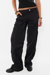 Pantalón cargo color arena de corte recto y tiro bajo, con recortes y presillas dobles en la cintura. Tiene acceso mediante cierre de nylon y botón personalizado, seis bolsillos laterales y dos en la espalda con tapa y botón snap a presión.