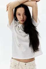 Remera blanca de algodón con cuello redondo y apliques de flores en el frente.