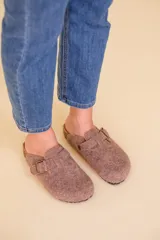 Sueco marrón de tejido tipo lana, con suela acolchonada y detalle de hebilla en la parte superior.