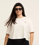 Remera blanca de algodón de corte crop, con cuello redondo, mangas cortas y moña de strass en el pecho.