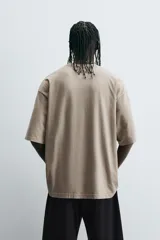 Camiseta color arena de corte holgado, cuello redondo y manga corta. Estampados combinados a contraste en delantero con textos e imágenes.
