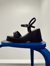 Sandalias negras de plataforma con tira ancha sobre el empeine y pulsera al tobillo con hebilla metálica.