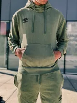 Buzo canguro de felpa con capucha y bolsillo canguro frontal. Color gris oscuro con efecto lavado o gastado, y logo Umbro en blanco en el pecho.