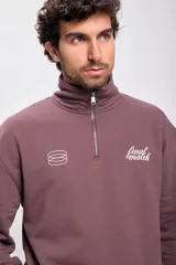 Buzo deportivo marrón con cuello alto y medio cierre frontal con cremallera. Tiene logo bordado en el pecho y puños y cintura acanalados.