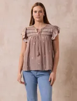 Blusa color marrón claro de algodón con bordados y calados blancos. Tiene cuello a la base, escote en V con lazo de ajuste y mangas cortas amplias.