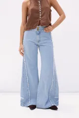 Pantalón de jean celeste de corte acampanado, con cintura alta y detalles desflecados en los laterales.
