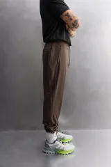 Pantalón de jogging color marrón oscuro, corte regular fit, confeccionado en tejido técnico ligero y elástico. Cuenta con cintura elástica ajustable con cordón, bolsillos frontales con cierre de cremallera, bolsillo trasero con cierre de cremallera oculta en costura y bajo ajustable con elástico.