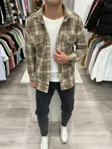 Sobrecamisa de paño a cuadros color tostado, con cuello clásico, cierre frontal con botones de madera, dos bolsillos de parche con solapa abotonada en el pecho y puños abotonados.
