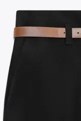 Pantalón marrón de tiro alto con cinturón negro, bolsillos delanteros y cierre frontal con cremallera y gancho metálico.