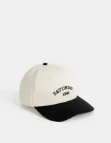 Gorra de béisbol bicolor, con visera negra y cuerpo blanco. Presenta bordado frontal con la leyenda "Saturday 1996".