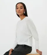 Blusa de tejido de punto color blanco, de manga larga, con puños diferenciados, escote redondo y detalles en hilo metalizado.