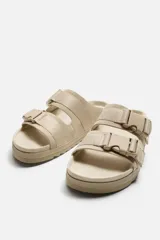 Sandalias planas color beige con doble tira ancha en el empeine y cierre con hebilla.