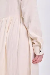 Vestido largo de muselina color crudo con bordado negro en el cuello y la pechera, corte evasé, manga larga y abotonadura frontal.