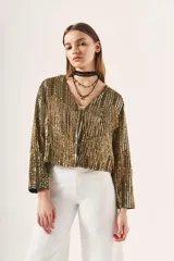 Saco corto dorado con flecos, bordado con lentejuelas y detalles en canutillo, con escote en V y mangas largas.